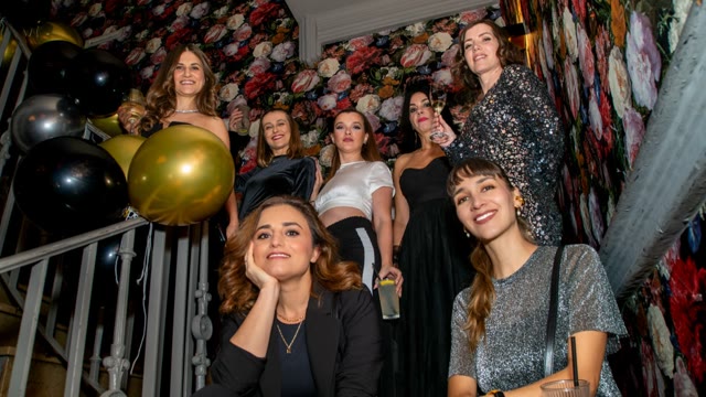 A group of colleagues poses laughing on a staircase between balloons and flowers