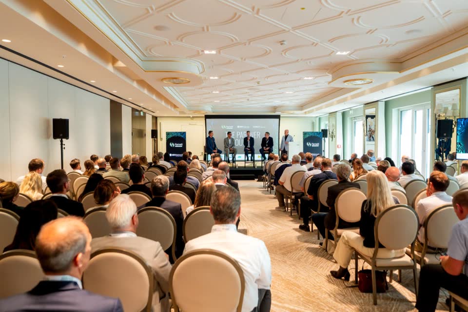 Audience in a hotel ballroom watching a panel on stage at a business conference