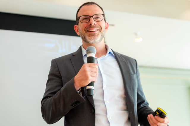 Speaker laughing as he talks into a microphone on stage