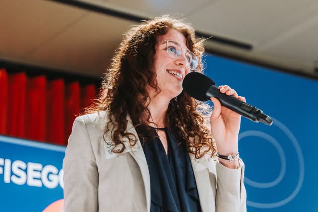 Speaker with curly hair smiling as she talks into a microphone
