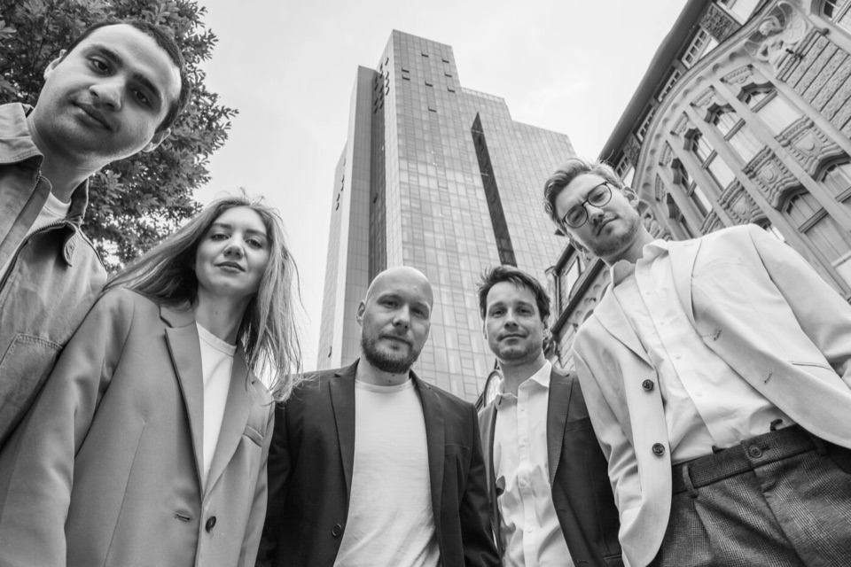 Schwarzweißes Gruppenfoto von unten: fünf Personen vor einem Hochhaus