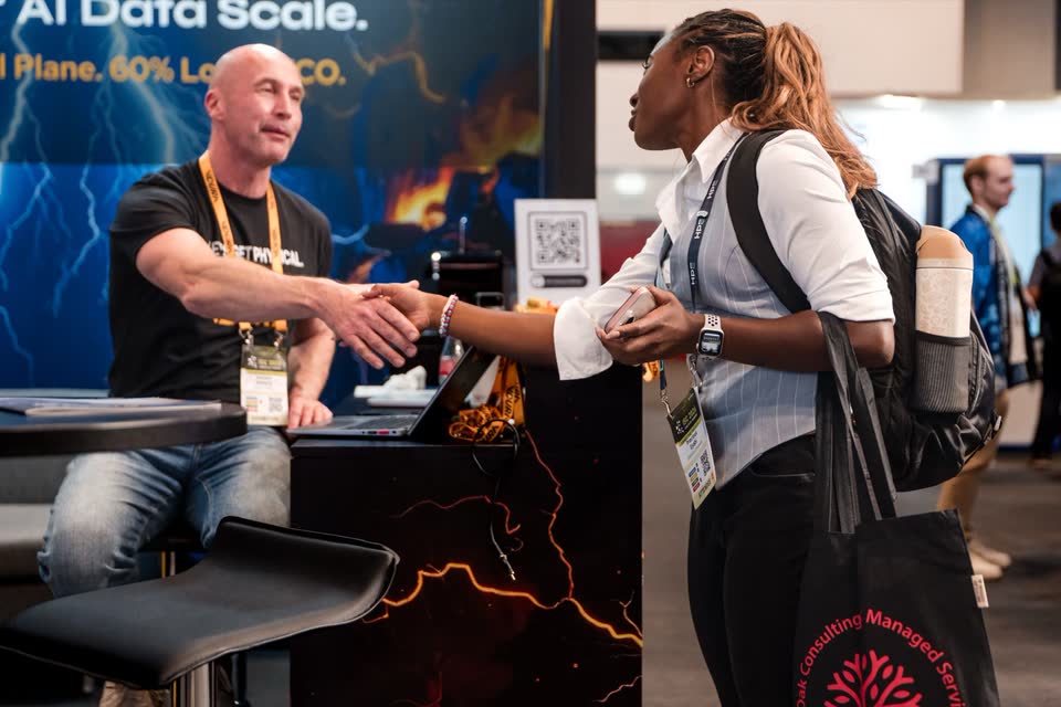 Ein Aussteller begrüßt eine Besucherin am Messestand mit Handschlag