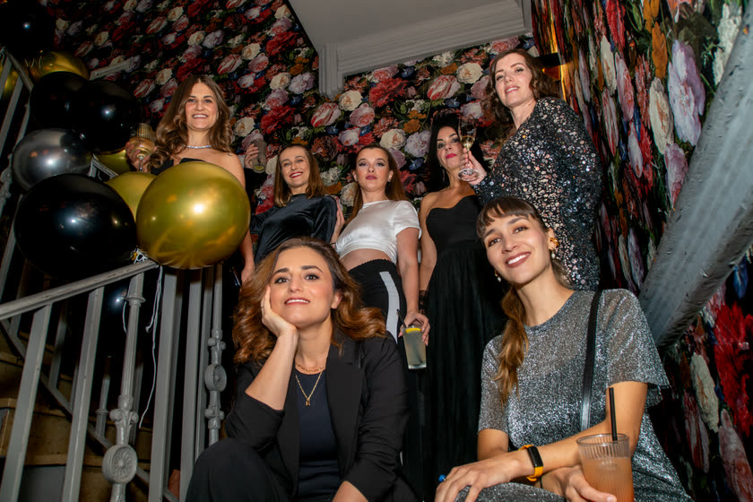 Eine Gruppe Gäste lächelt auf einer Treppe neben goldenen Ballons