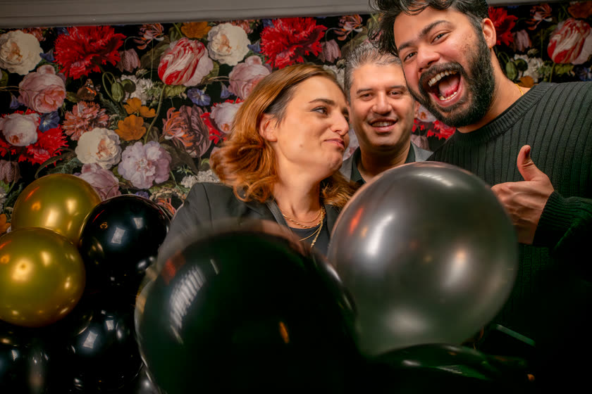 Gäste lachen laut zwischen schwarzen und goldenen Ballons