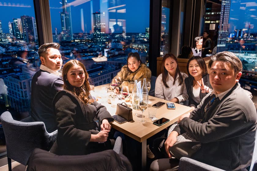 Gäste lächeln an einem Dinnertisch vor den Lichtern der Stadt